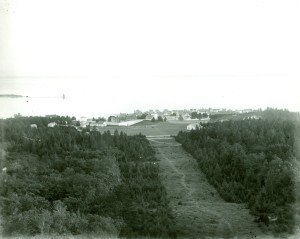 View of Fort Mackinac from Fort Holmes, ca. 1900. A portion of the grandstand is visible at the far left of the parade ground.  Sergeants’ Quarters and the roof of Mon-commissioned Officers’ Quarters are visible at the bottom right of the parade ground.  