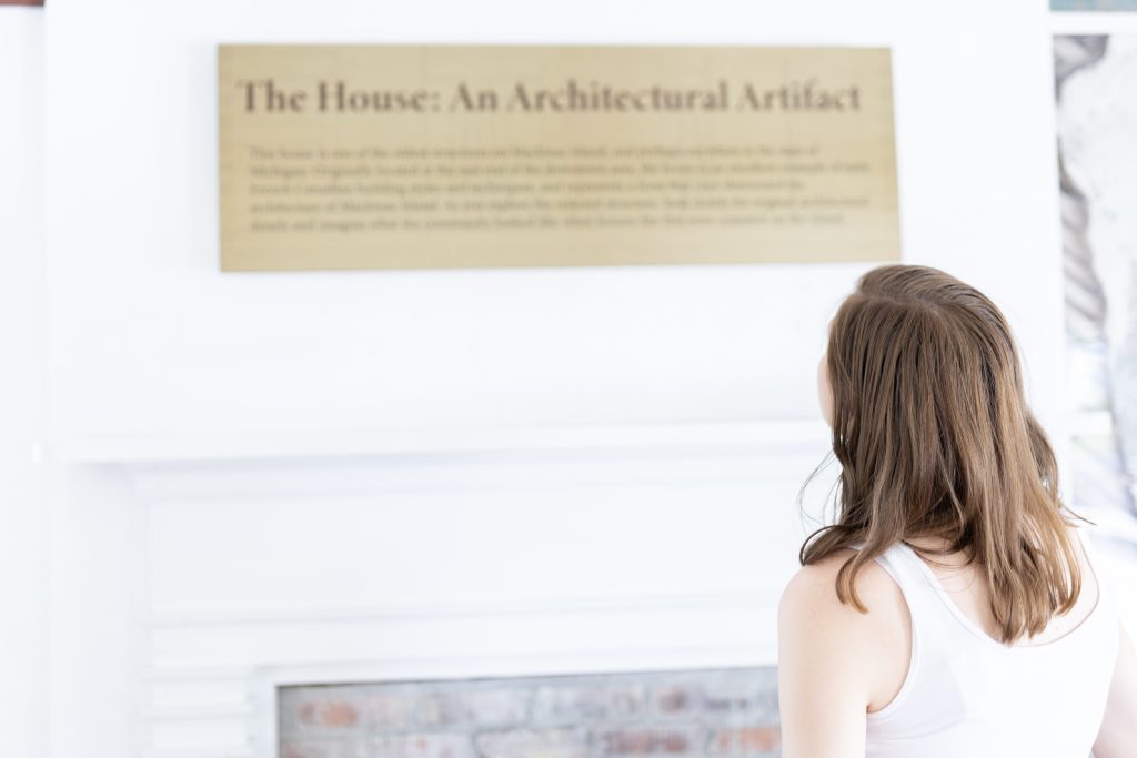 A person reading a tan exhibit panel describing the McGulpin House, located on Mackinac Island, as an architectural artifact.