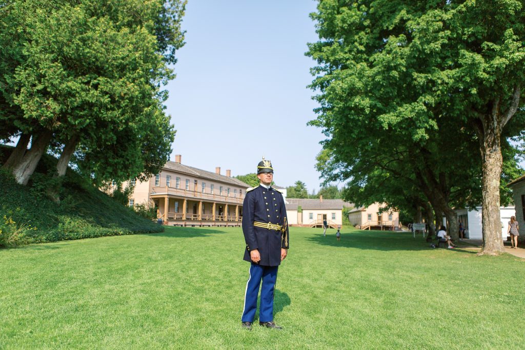 A soldier in dress uniform standing on the parade ground at Fort Mackinac.