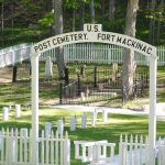 Cemetery surrounded by a white picket fence with an archway reading the words "U.S. Post Cemetery, Fort Mackinac"