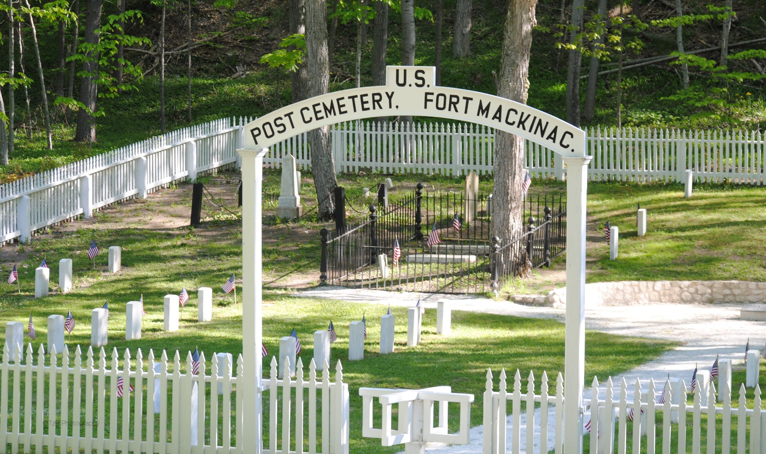Cemetery surrounded by a white picket fence with an archway reading the words "U.S. Post Cemetery, Fort Mackinac"