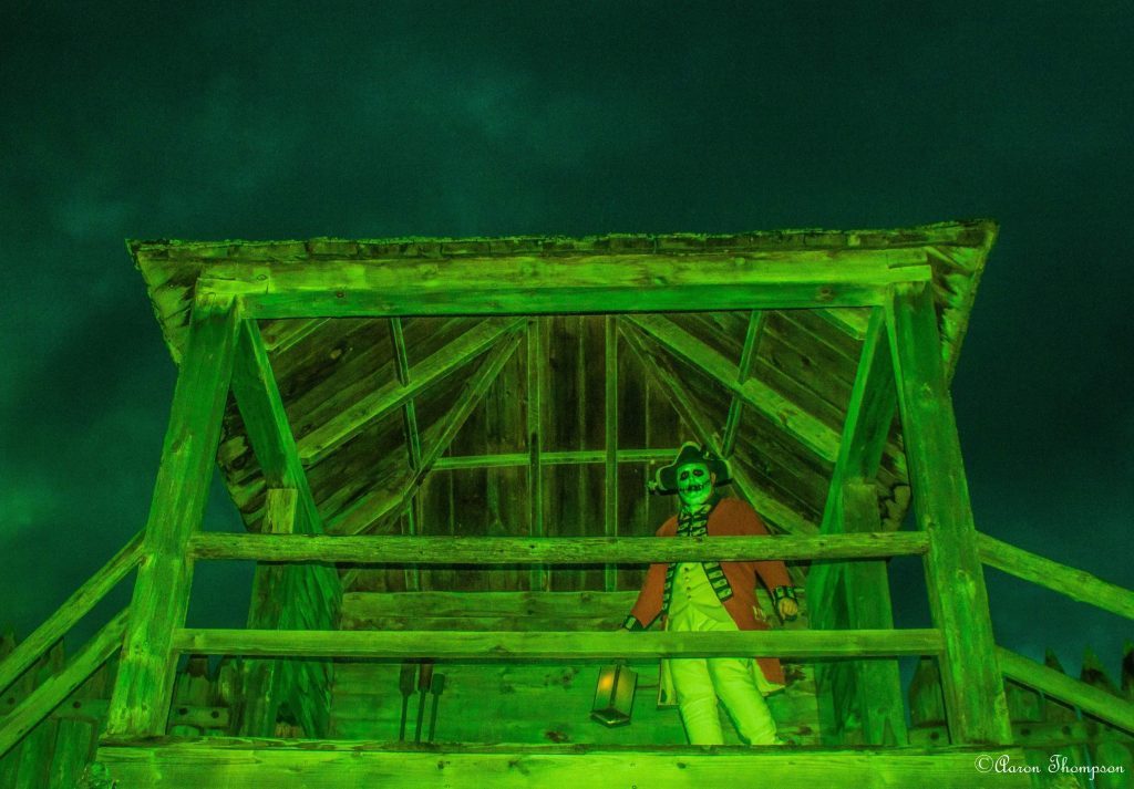 A wooden building, glowing green, with a British soldier dressed up as a skeleton.