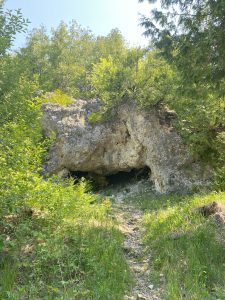 A large gray rock mass known as Skull Cave with trees and bushes surrounding it. 