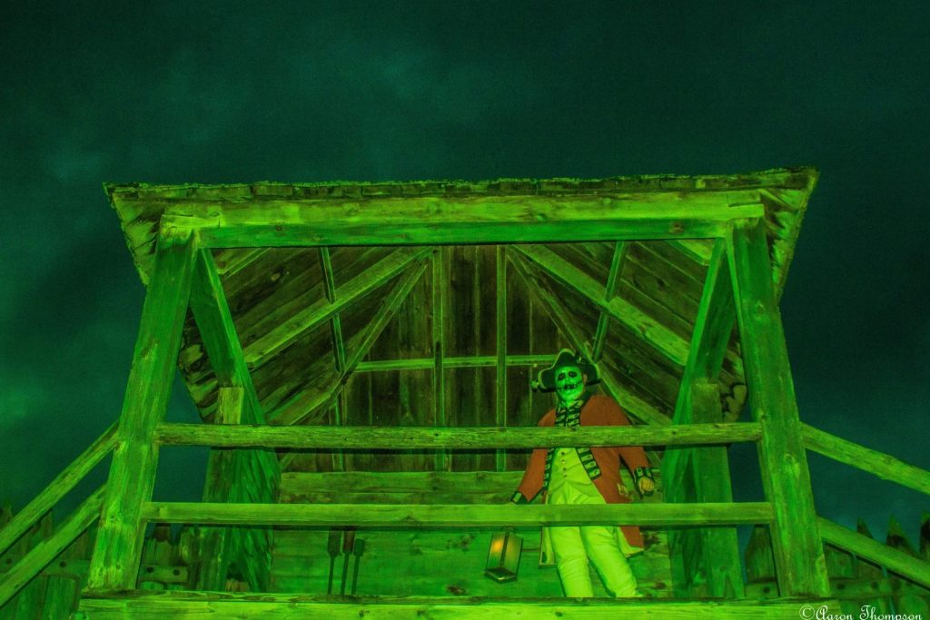 A wooden building, glowing green, with a British soldier dressed up as a skeleton.